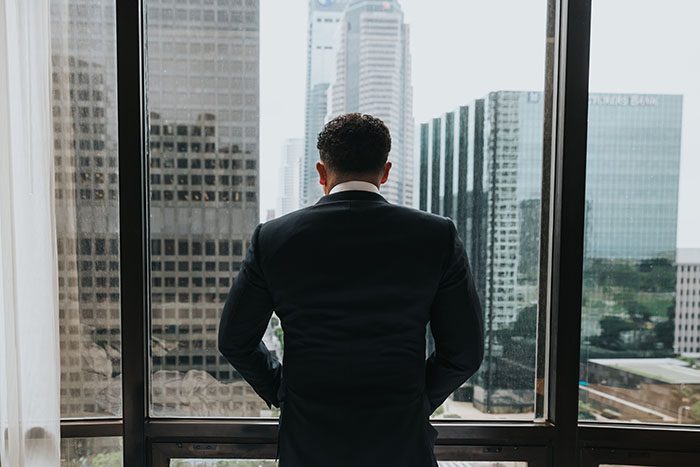 A successful professional standing at a window, weighing a difficult decision